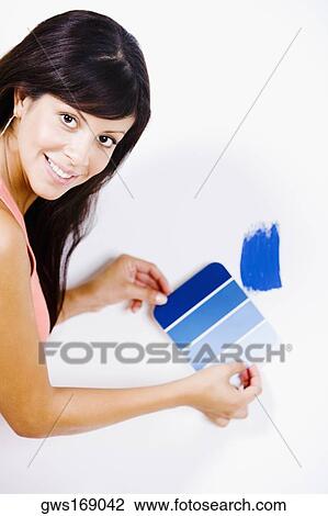Stock Image - Portrait of a young woman holding a color swatch against a wall. Fotosearch