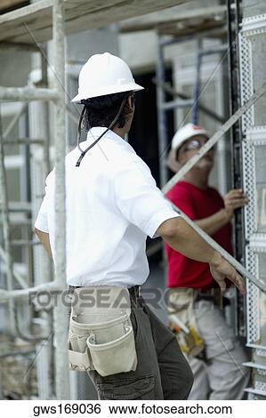 Stock Photograph - Side profile of a male architect working at a construction site with another male architect standing beside him. Fotosearch