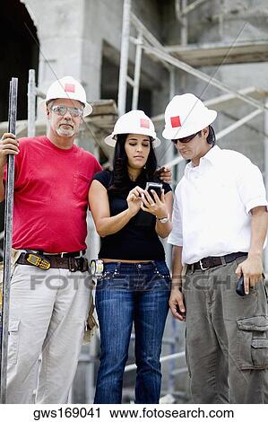 Stock Image - Two male and a female architects standing at a construction site. Fotosearch