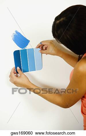 Stock Image - Woman holding a color swatch against a wall. Fotosearch