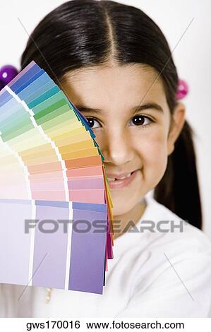 Stock Photograph - Portrait of a girl with color swatches in front of her face and smiling. Fotosearch