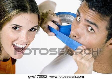 Stock Image - Portrait of a mid adult woman sticking an adhesive tape on a young man's mouth. Fotosearch