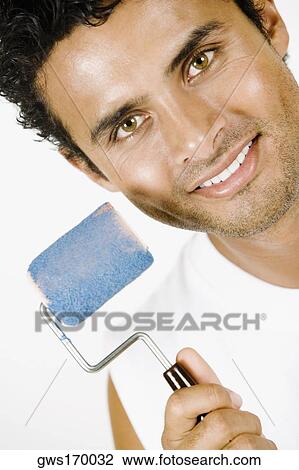 Stock Image - Portrait of a young man holding a paint roller and smiling. Fotosearch