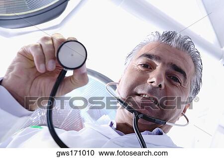 Low angle view of a male doctor holding a stethoscope View Large Photo Image Stock Image - Low angle view of a male doctor holding a stethoscope. Fotosearch