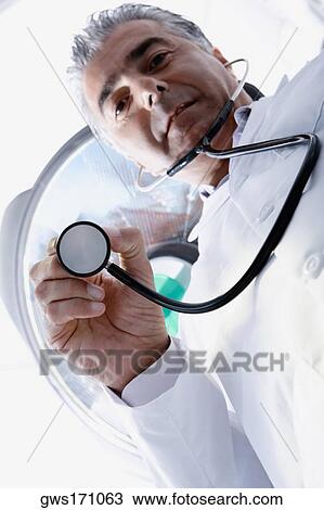 Stock Image - Low angle view of a male doctor holding a stethoscope. Fotosearch