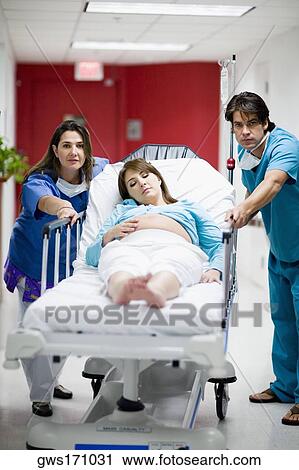 Male and a female doctor pushing a pregnant young woman lying on a