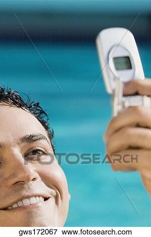 Close-up of a young man holding a mobile phone and smiling View Large Photo Image Stock Photo - Close-up of a young man holding a mobile phone and smiling. Fotosearch
