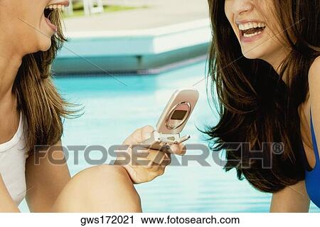 Close-up of a young woman holding a mobile phone and smiling with her friend View Large Photo Image Stock Image - Close-up of a young woman holding a mobile phone and smiling with her friend. Fotosearch