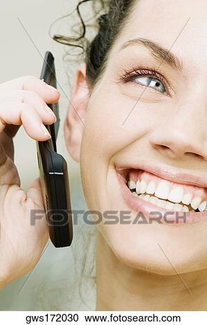 Close-up of a young woman holding a mobile phone and smiling View Large Photo Image Stock Image - Close-up of a young woman holding a mobile phone and smiling. Fotosearch