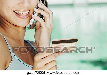 Close-up of a young woman holding a credit card and talking on a mobile phone View Large Photo Image Stock Photography - Close-up of a young woman holding a credit card and talking on a mobile phone. Fotosearch