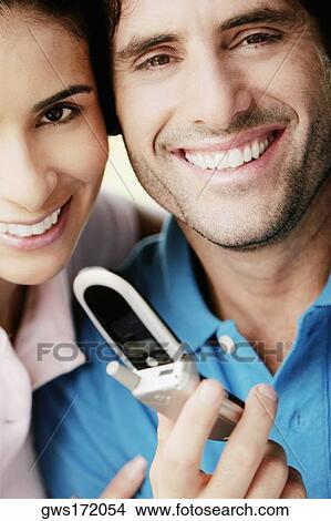Portrait of a young man holding a mobile phone and smiling with a young woman View Large Photo Image Picture - Portrait of a young man holding a mobile phone and smiling with a young woman. Fotosearch