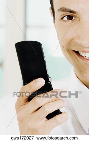 Portrait of a young man holding a mobile phone and smiling View Large Photo Image Stock Photo - Portrait of a young man holding a mobile phone and smiling. Fotosearch
