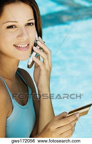 Portrait of a young woman holding a credit card and using a mobile phone View Large Photo Image Stock Photograph - Portrait of a young woman holding a credit card and using a mobile phone. Fotosearch