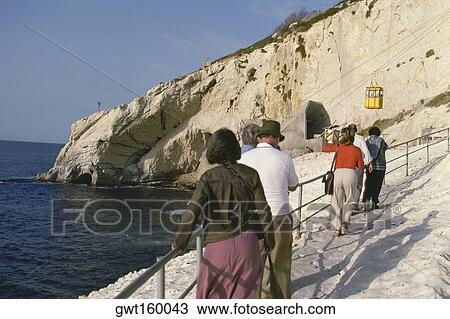 Stock Image - Rear view of a group of tourists walking towards an overhead cable car station, Israel. Fotosearch