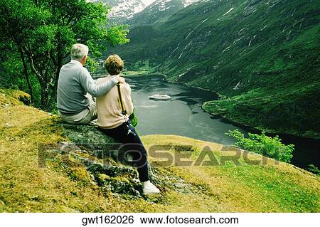 Rear view of two people sitting near a river, Geiranger Fjord, Norway View Large Photo Image Stock Photograph - Rear view of two people sitting near a river, Geiranger Fjord, Norway. Fotosearch