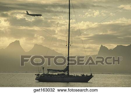 Stock Image - Airplane flying over a sailboat, Moorea, Tahiti, Society Islands, French Polynesia. Fotosearch