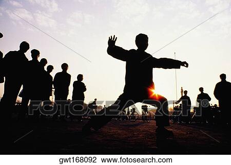 Silhouette of a man practicing tai chi with a group of people standing behind him, Xian, China View Large Photo Image Stock Image - Silhouette of a man practicing tai chi with a group of people standing behind him, Xian, China. Fotosearch