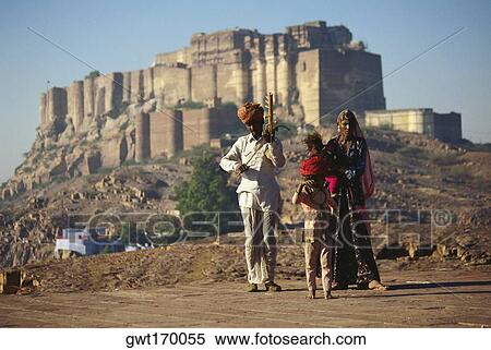 Stock Photography - Mid adult man playing a musical instrument with his wife and children walking beside him, Jodhpur, Rajasthan, India. Fotosearch
