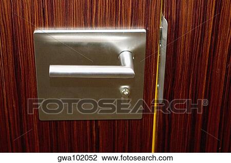 Stock Image - Close-up of a steel door handle on a closed wooden door. Fotosearch