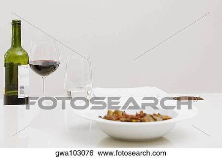 Close-up of a wine bottle with a glass of red wine and a bowl on a dining table View Large Photo Image Stock Photograph - Close-up of a wine bottle with a glass of red wine and a bowl on a dining table. Fotosearch