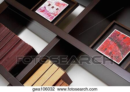 Stock Image - Close-up of books and picture frames in shelves. Fotosearch