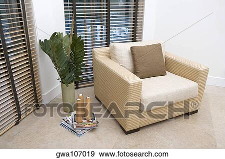 Stock Photo - Armchair with decorative paper weights on magazines in a living room. Fotosearch