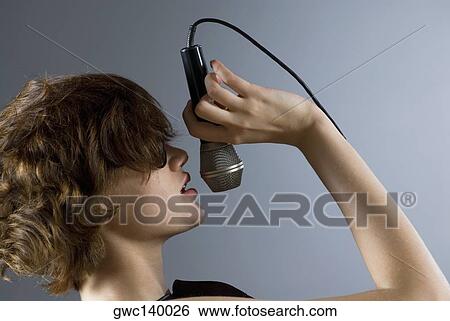 Close-up of a young woman singing into a microphone View Large Photo Image Stock Photograph - Close-up of a young woman singing into a microphone. Fotosearch