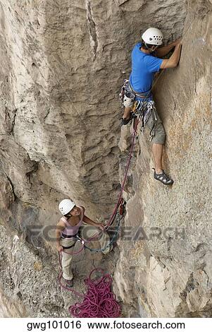 Female rock climber looking at a male rock climber scaling a rock face View Large Photo Image Stock Photograph - Female rock climber looking at a male rock climber scaling a rock face. Fotosearch