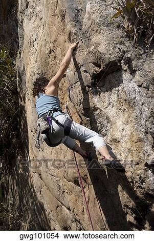 Low angle view of a female rock climber scaling a rock face View Large Photo Image Picture - Low angle view of a female rock climber scaling a rock face. Fotosearch