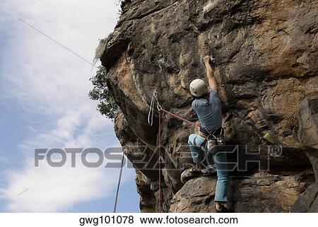 Low angle view of a female rock climber scaling a rock face View Large Photo Image Stock Photo - Low angle view of a female rock climber scaling a rock face. Fotosearch