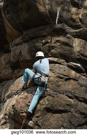 Low angle view of a female rock climber scaling a rock face View Large Photo Image Stock Photograph - Low angle view of a female rock climber scaling a rock face. Fotosearch