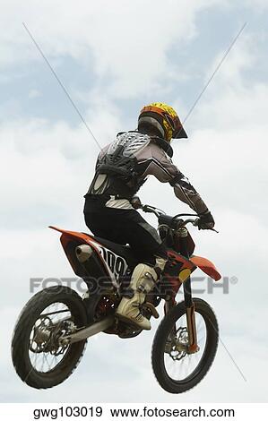 Low angle view of a motocross rider performing a jump on a motorcycle View Large Photo Image Stock Photo - Low angle view of a motocross rider performing a jump on a motorcycle. Fotosearch