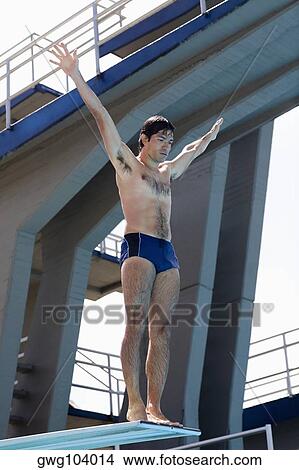 Picture - Low angle view of a mid adult man taking start from a diving platform. Fotosearch