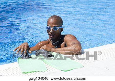 Stock Photograph - Mid adult man drying his flippers at the ledge of a swimming pool. Fotosearch