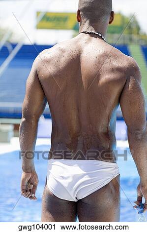 Stock Image - Rear view of a mid adult man standing at the poolside and holding swimming goggles. Fotosearch