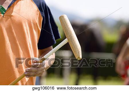 Stock Photograph - Mid section view of a man holding a polo mallet. Fotosearch