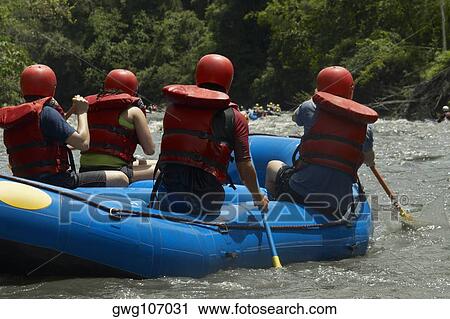 Stock Image - Rear view of four people rafting in a river. Fotosearch
