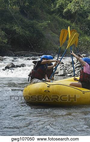 Stock Image - Side profile of four people rafting in a river. Fotosearch