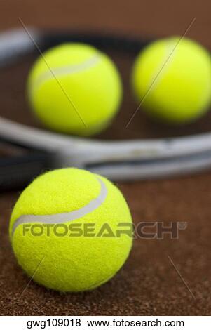 Stock Photo - Close-up of three tennis balls and a racket in a court. Fotosearch