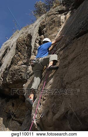 Low angle view of a male rock climber scaling a rock face View Large Photo Image Stock Image - Low angle view of a male rock climber scaling a rock face. Fotosearch