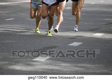 Stock Image - Low section view of male athletes running on a road. Fotosearch