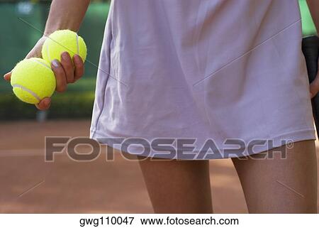 Stock Photo - Mid section view of a young woman holding two tennis balls. Fotosearch