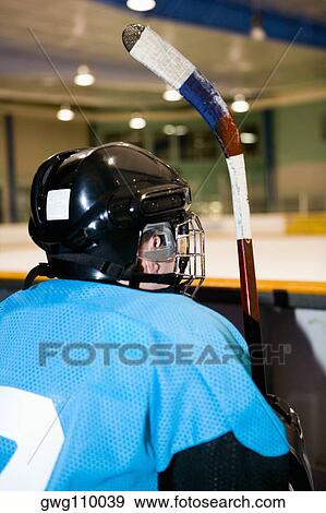 Stock Photo - Rear view of an ice hockey player sitting next to the railing of an ice rink. Fotosearch