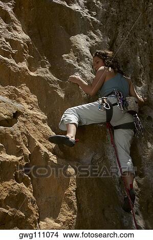 Low angle view of a female rock climber scaling a rock face View Large Photo Image Picture - Low angle view of a female rock climber scaling a rock face. Fotosearch