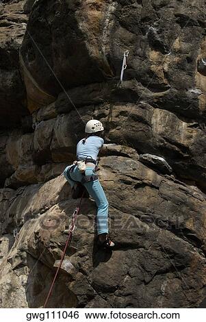 Low angle view of a female rock climber scaling a rock face View Large Photo Image Stock Photograph - Low angle view of a female rock climber scaling a rock face. Fotosearch