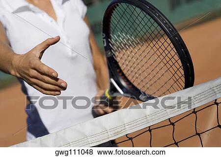 Stock Photo - Mid section view of a young woman holding a tennis racket and reaching out for a handshake. Fotosearch