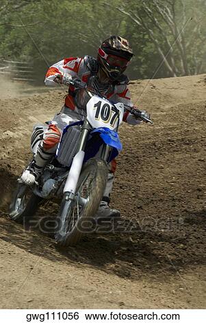 Stock Photograph - Motocross rider riding a motorcycle on a dirt road. Fotosearch