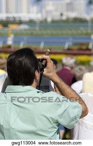 Rear view of a spectator looking through a pair of binoculars at the horseracing track View Large Photo Image Picture - Rear view of a spectator looking through a pair of binoculars at the horseracing track. Fotosearch