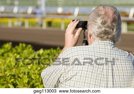 Rear view of a spectator looking through a pair of binoculars at the horseracing track View Large Photo Image Stock Image - Rear view of a spectator looking through a pair of binoculars at the horseracing track. Fotosearch