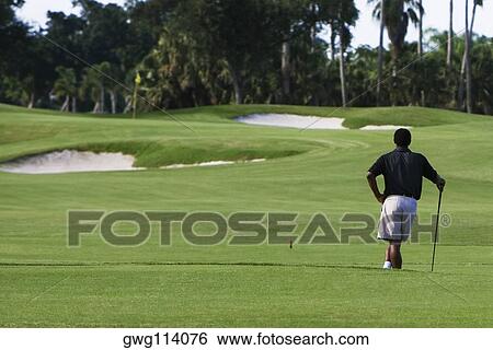 Rear view of a man standing with a golf club in a golf course View Large Photo Image Stock Photograph - Rear view of a man standing with a golf club in a golf course. Fotosearch